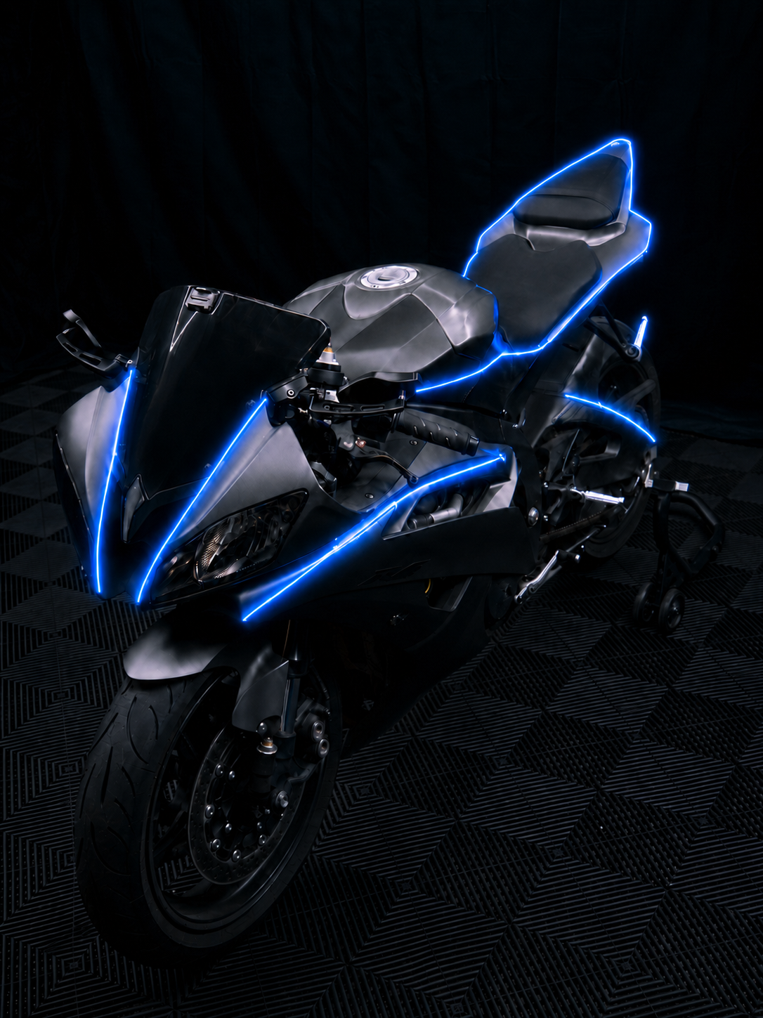 Black sport bike in a dark studio with blue NYTRON contour lighting tracing the fairing, tank, seat and tail.